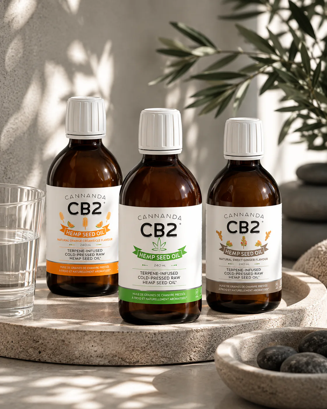 Three bottles of Cannanda CB2 Hemp Seed Oil, Orange Creamsicle, Original and Sweet Ginger, on a stone tray in the sun